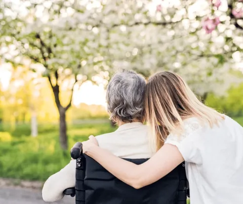 Caregiver supporting an older adult in a wheelchair outdoors
